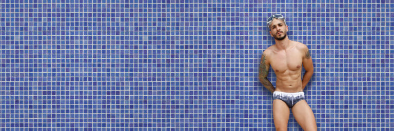 hombre usando traje de baño parado frente una pared de azulejos color azul